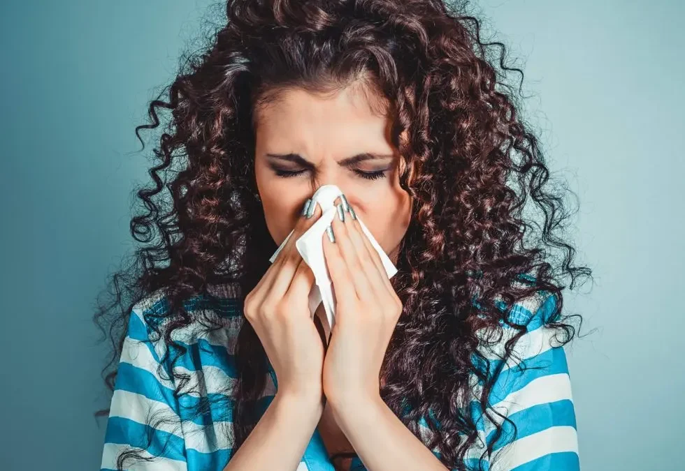 Woman sneezing into a tissue, representing seasonal allergy relief and respiratory health.