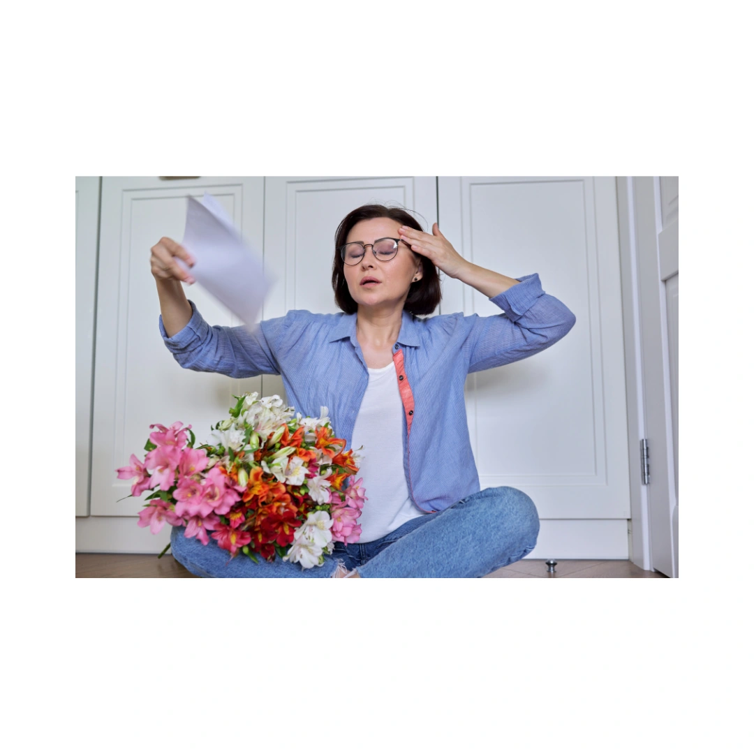 Woman fanning herself while sitting with flowers, representing menopause and hormonal balance.