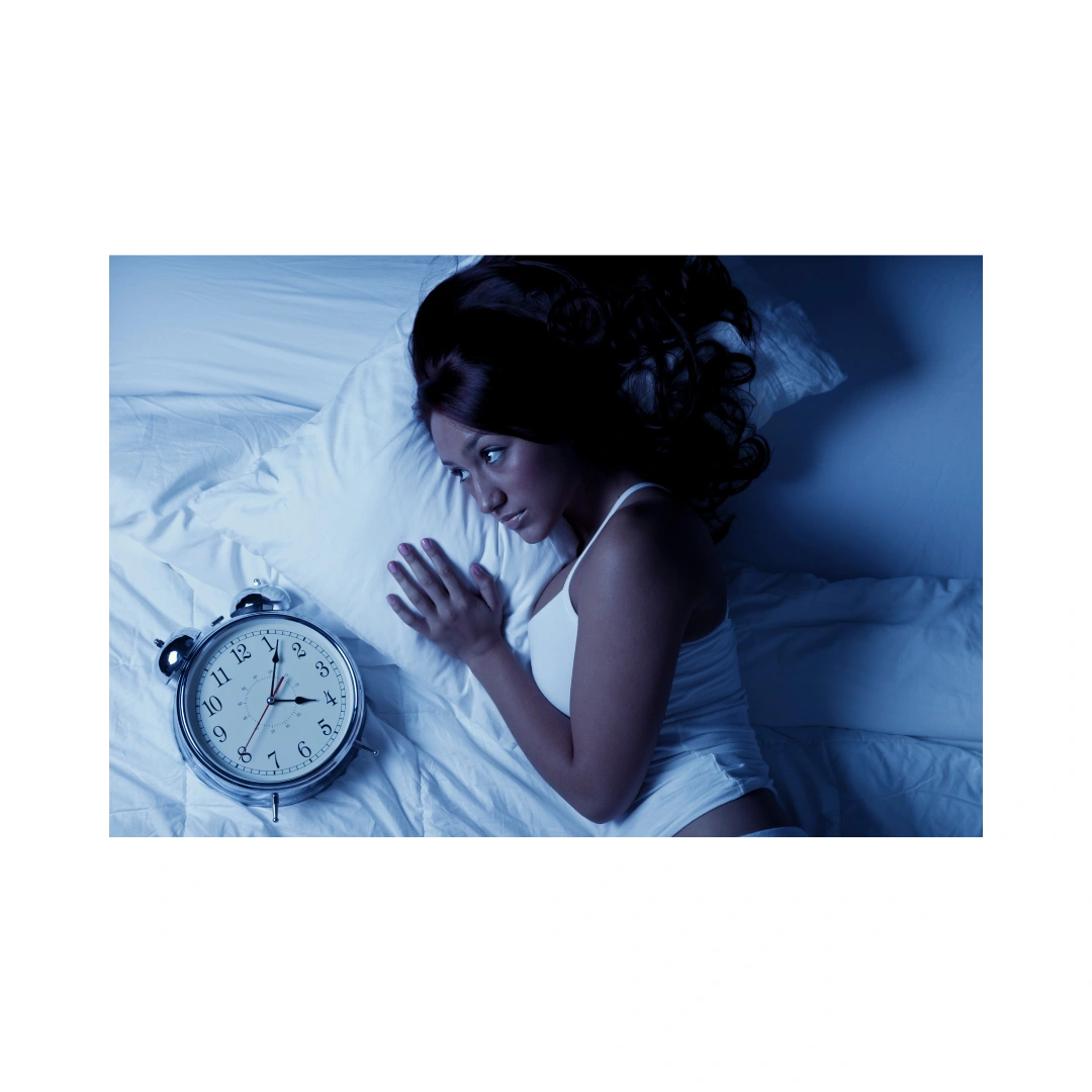 Woman lying awake in bed next to an alarm clock, representing insomnia and sleep health.
