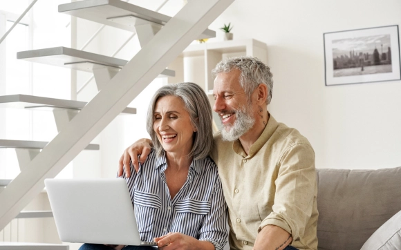 Senior couple laughing while using a laptop together for telehealth or health research.