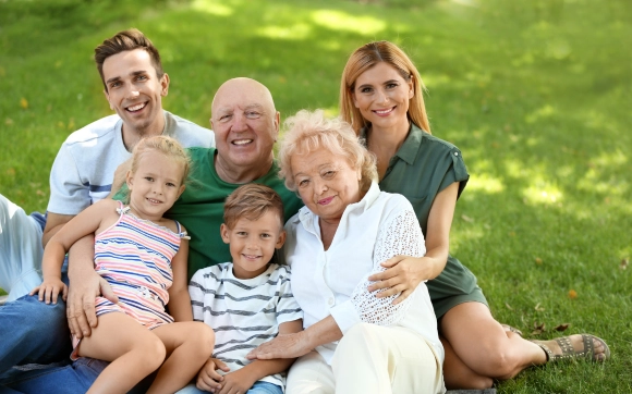 Happy family of three generations sitting together on grass, representing community health.
