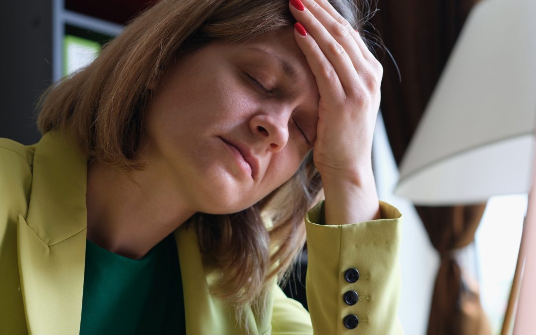 Overworked woman sitting in office and touching head with hand