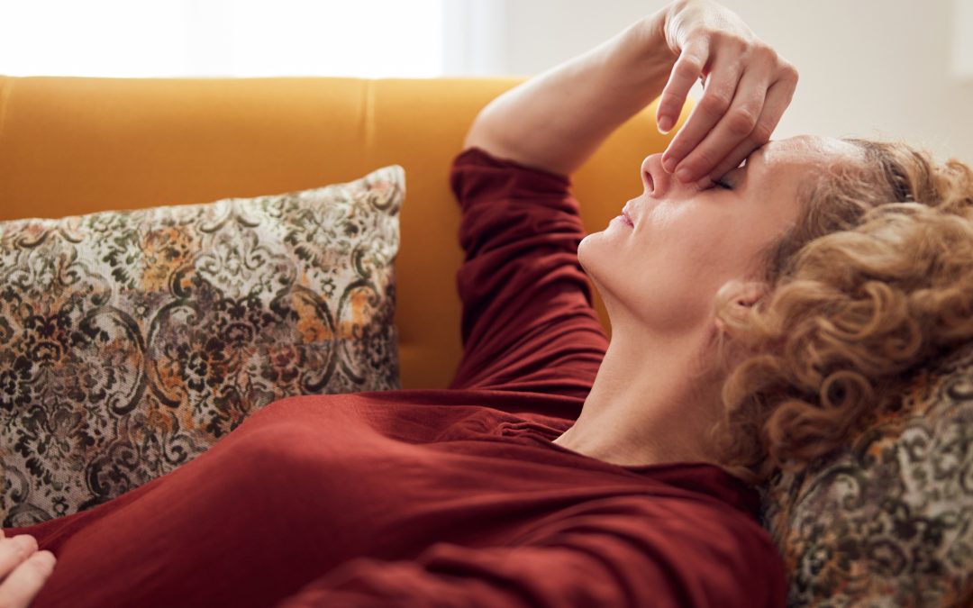 A woman lies on a couch with her eyes closed, pinching the bridge of her nose in discomfort.