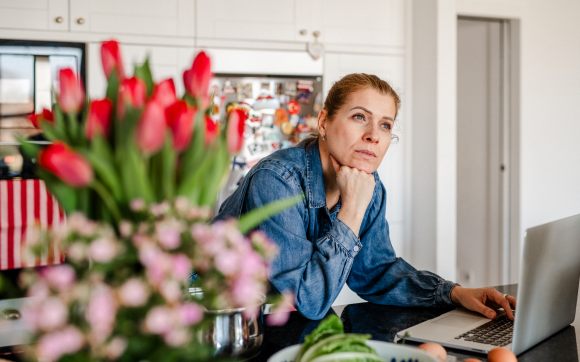 Midlife woman standing thoughtfully in her kitchen in soft morning light, contemplating her body and her health