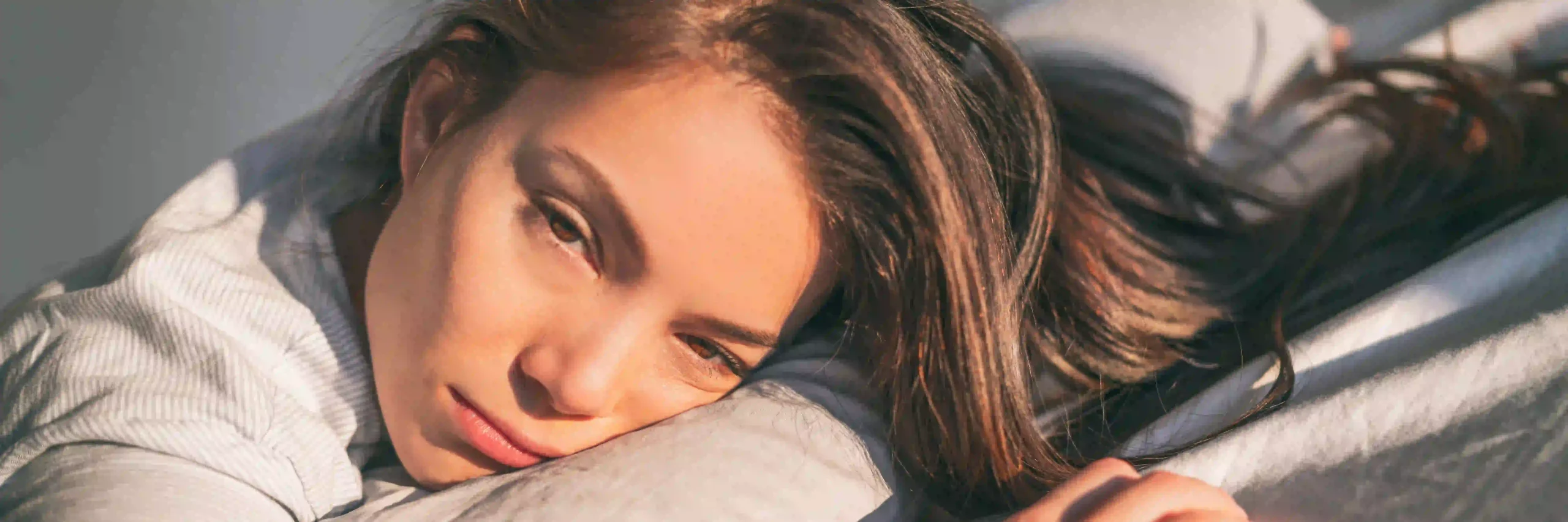 Close-up of a thoughtful woman lying on a pillow in morning sunlight